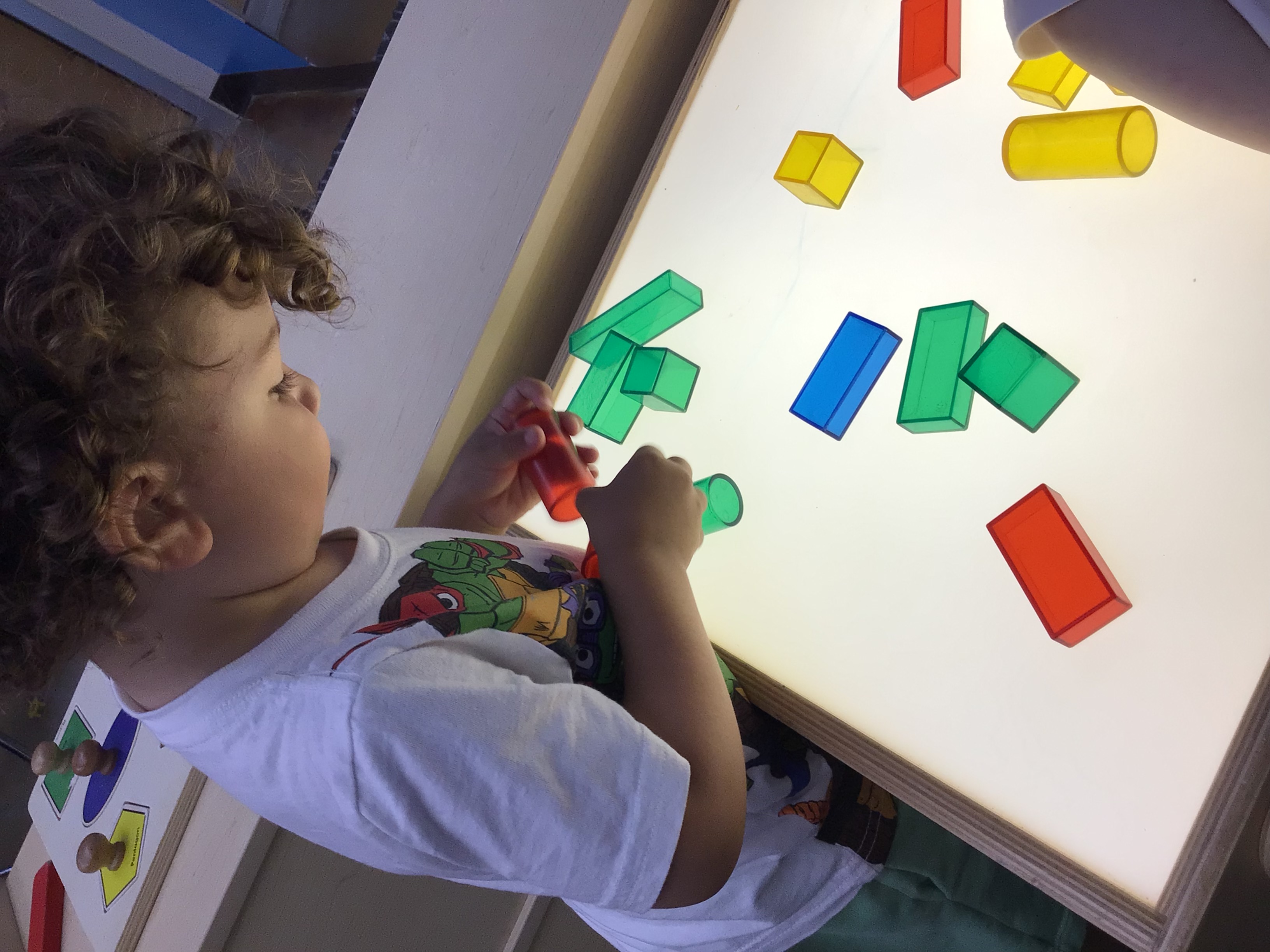 Kid looking at transparent 3d shapes on a lightbox.