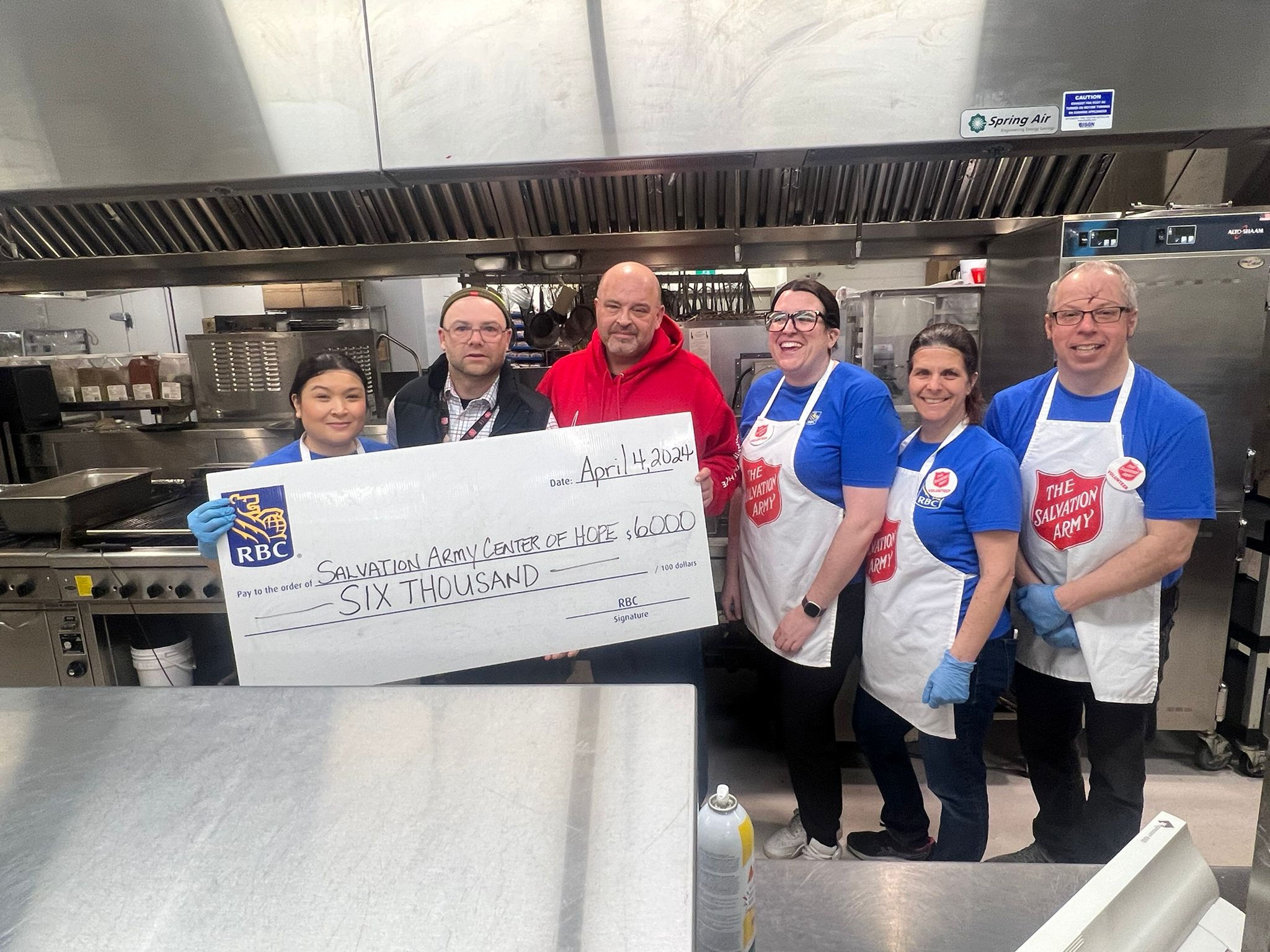 A group of volunteers from RBC wearing a salvation army apron and 2 staff of the WCOH receiving a big cheque from RBC